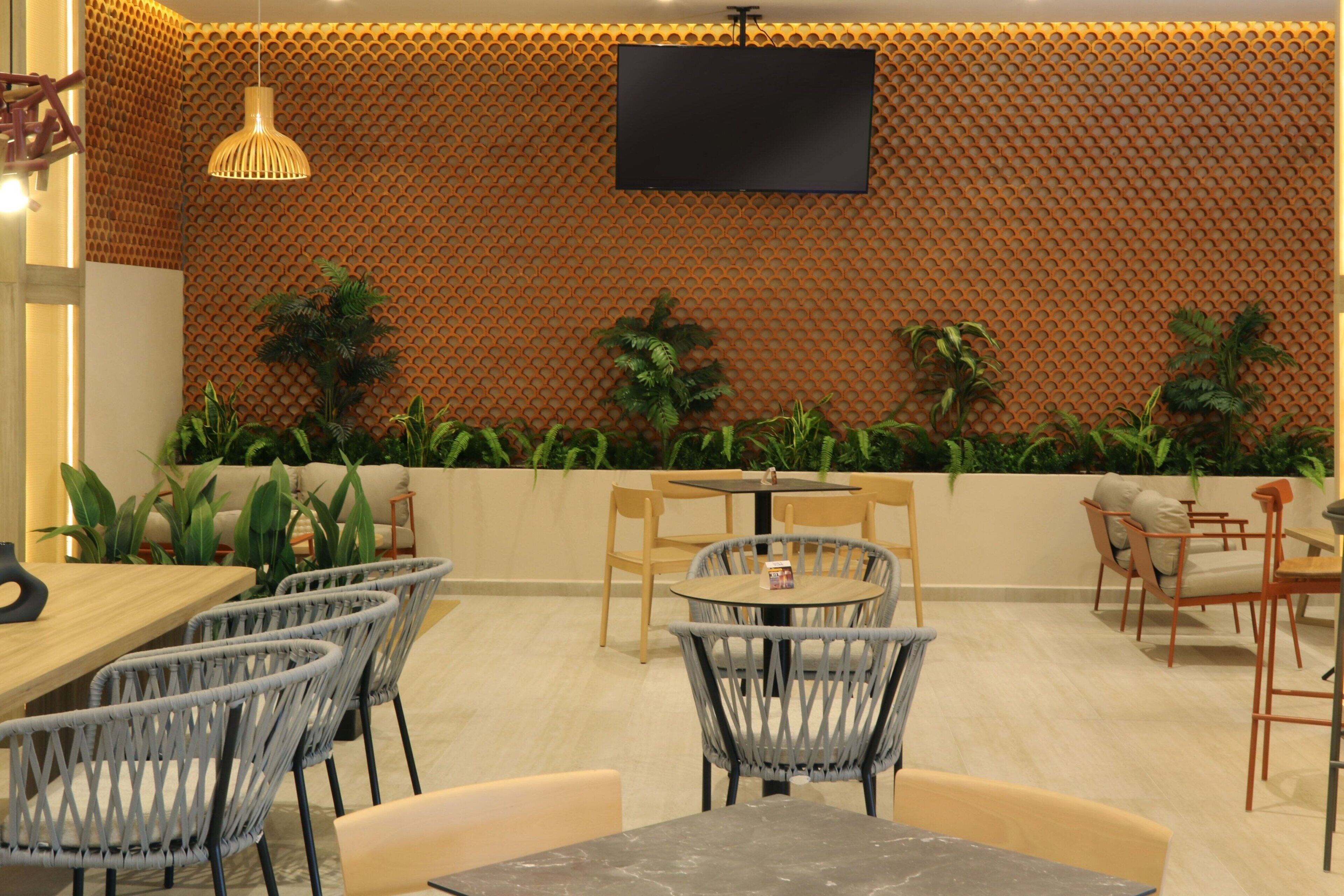 Un espace de détente intérieur moderne, doté d’un mur décoré de motifs, d’un téléviseur à écran plat, ainsi que de plusieurs tables et chaises.
