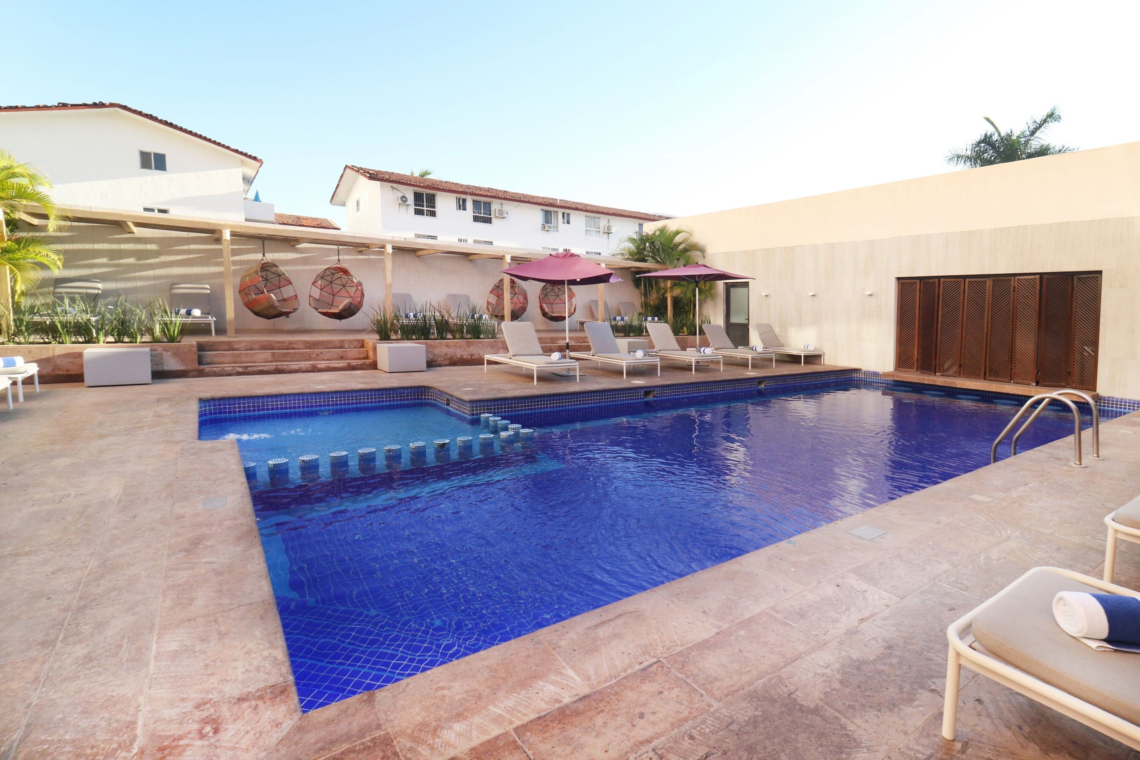A swimming pool with lounge chairs and umbrellas, surrounded by a building with a tiled roof and a mural.