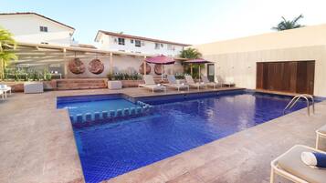 A swimming pool with lounge chairs and umbrellas, surrounded by a building with a tiled roof and a mural.
