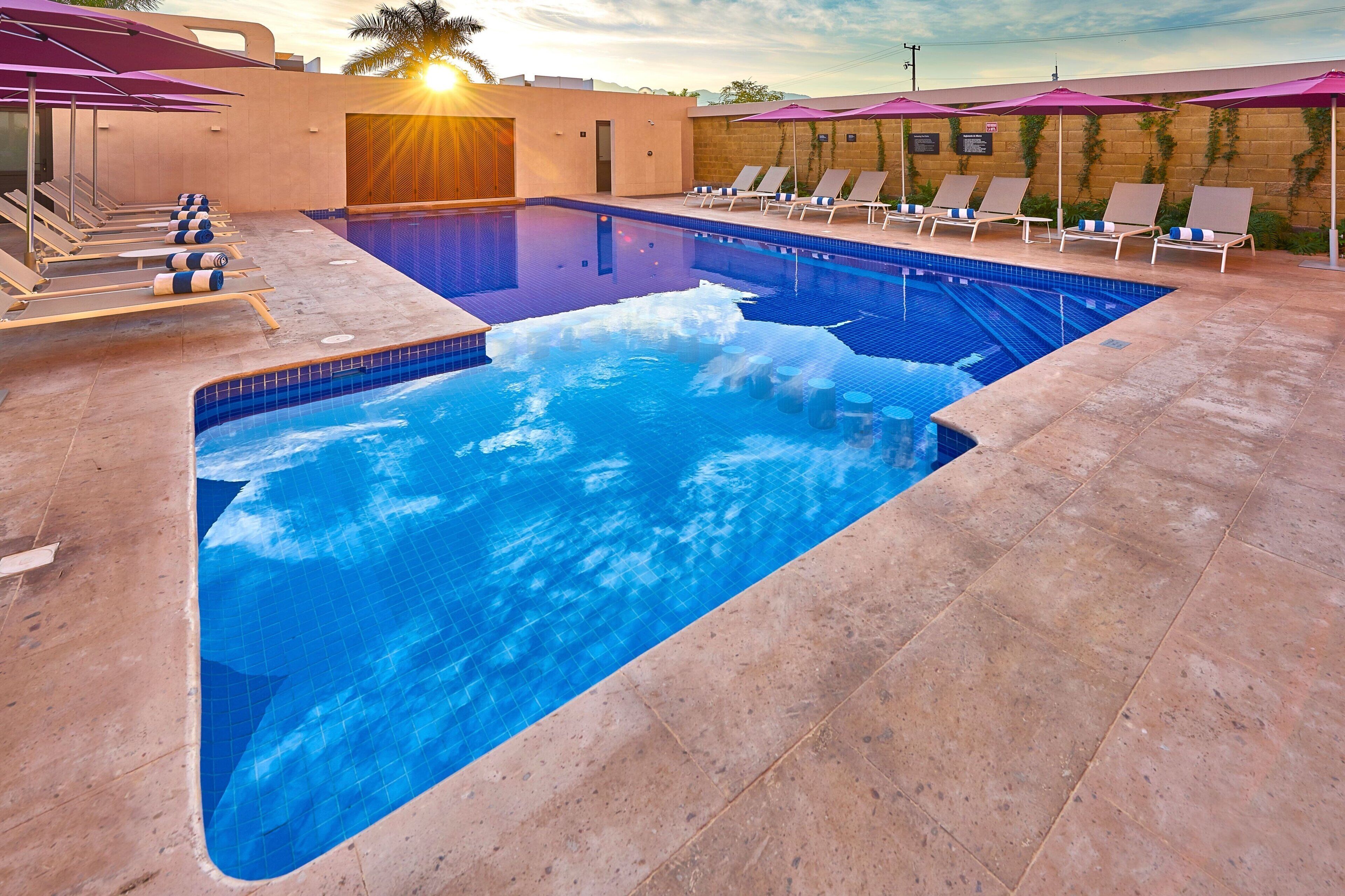 A swimming pool with lounge chairs and umbrellas, surrounded by a tiled deck.