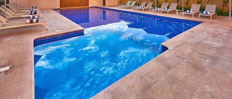 A swimming pool with lounge chairs and umbrellas, surrounded by a tiled deck.