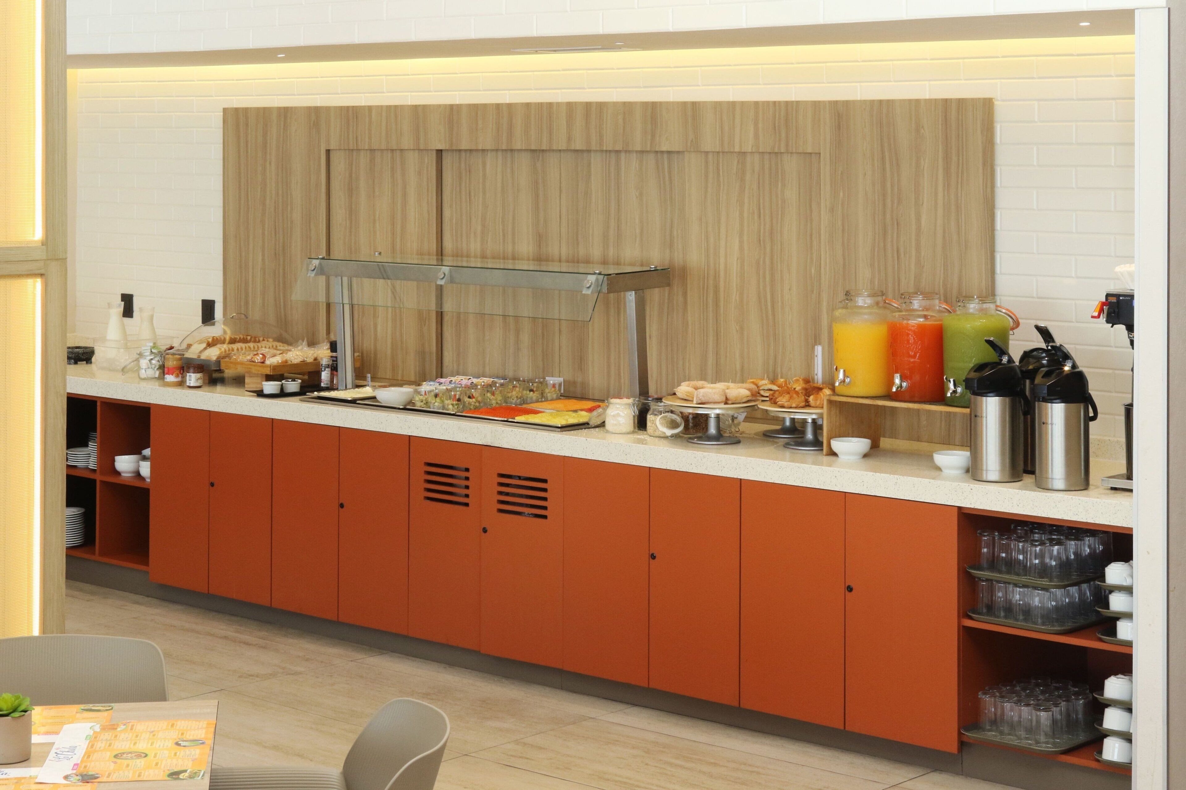 A breakfast bar with a variety of food items, a juice station, and kitchen appliances.