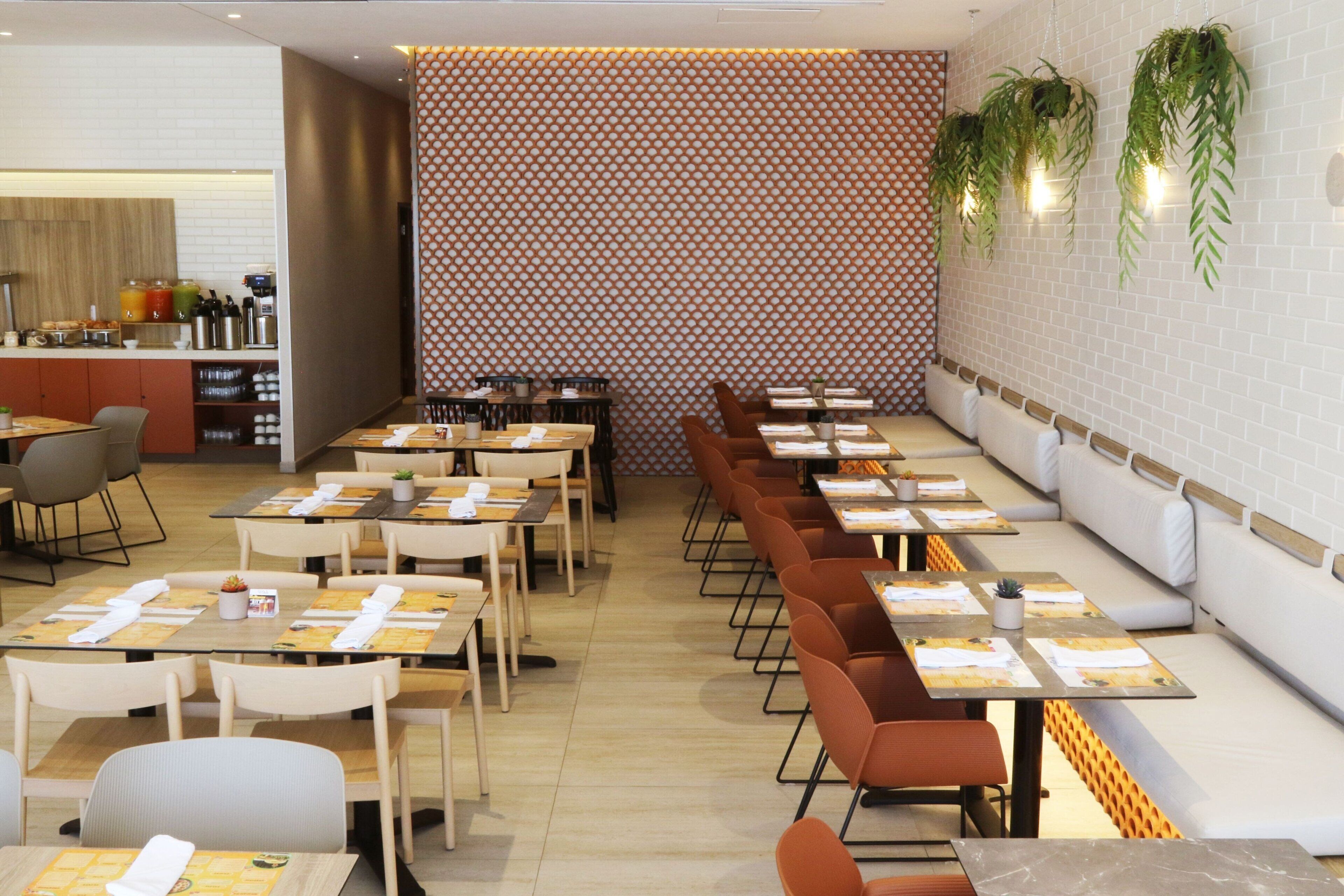 Un restaurant doté de nombreuses tables et de banquettes, d’un mur orné de motifs et de plantes suspendues.