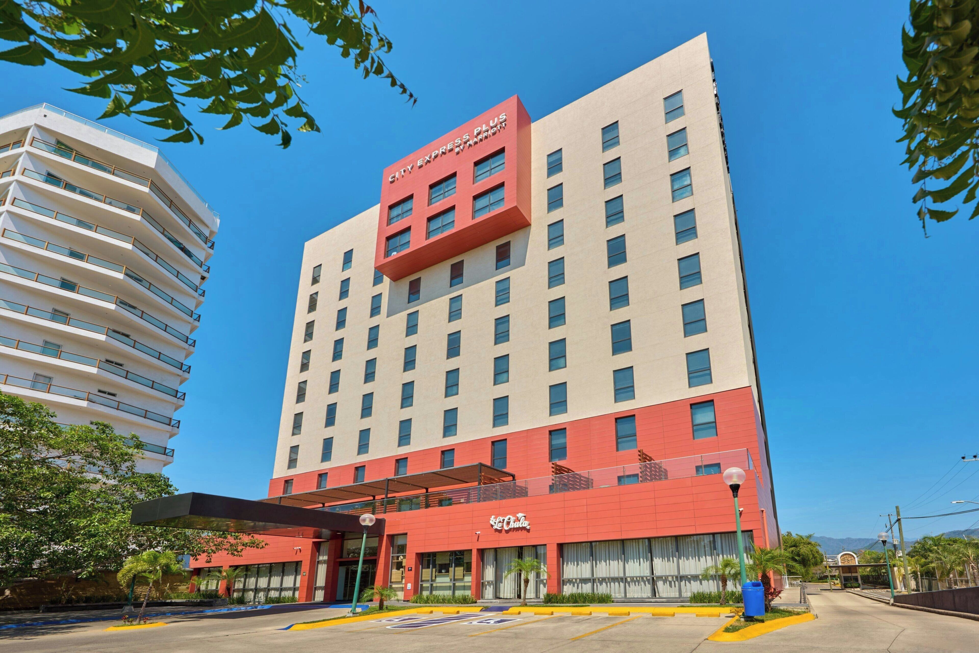 A multi-story hotel with a red and white facade, a covered entrance, and a visible restaurant named 'El Cholo' at the ground level.