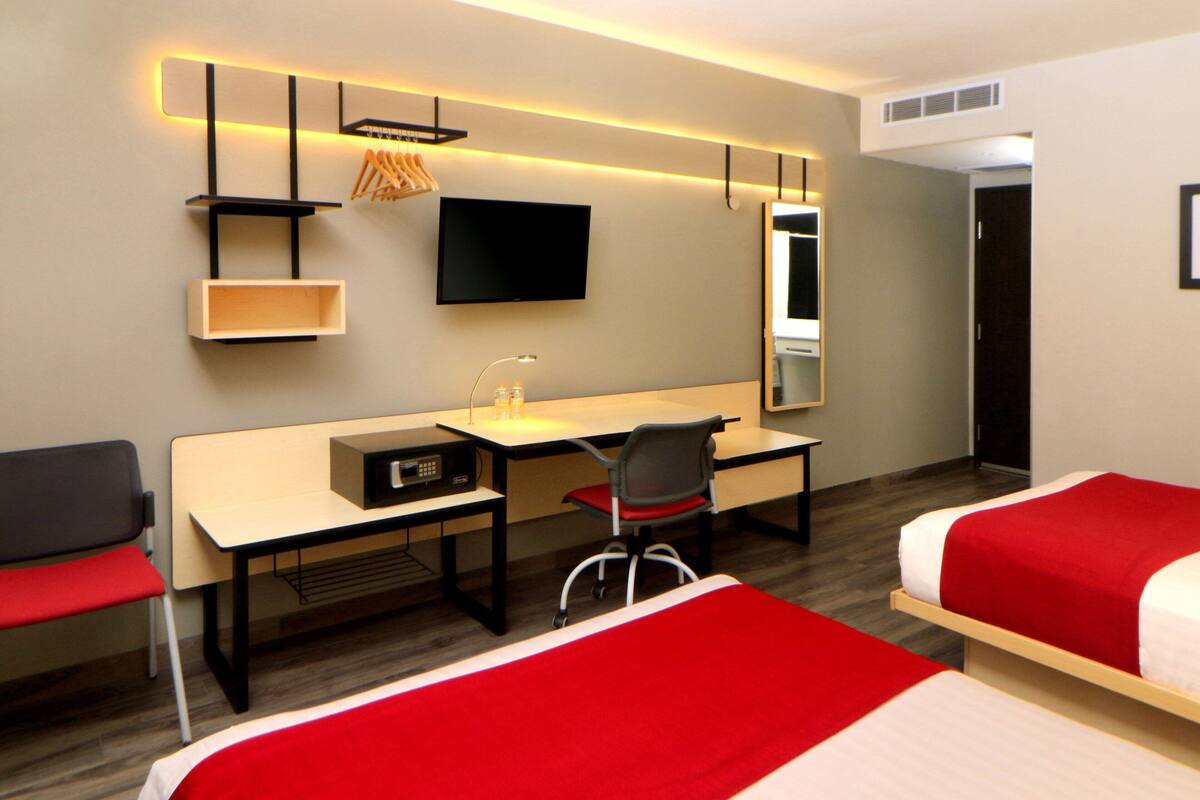 A hotel room with a desk, chair, two beds, a TV, and a mirror.