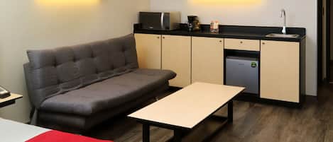 A compact hotel room with a sofa, a small table, a microwave, a coffee maker, and a mini-fridge.