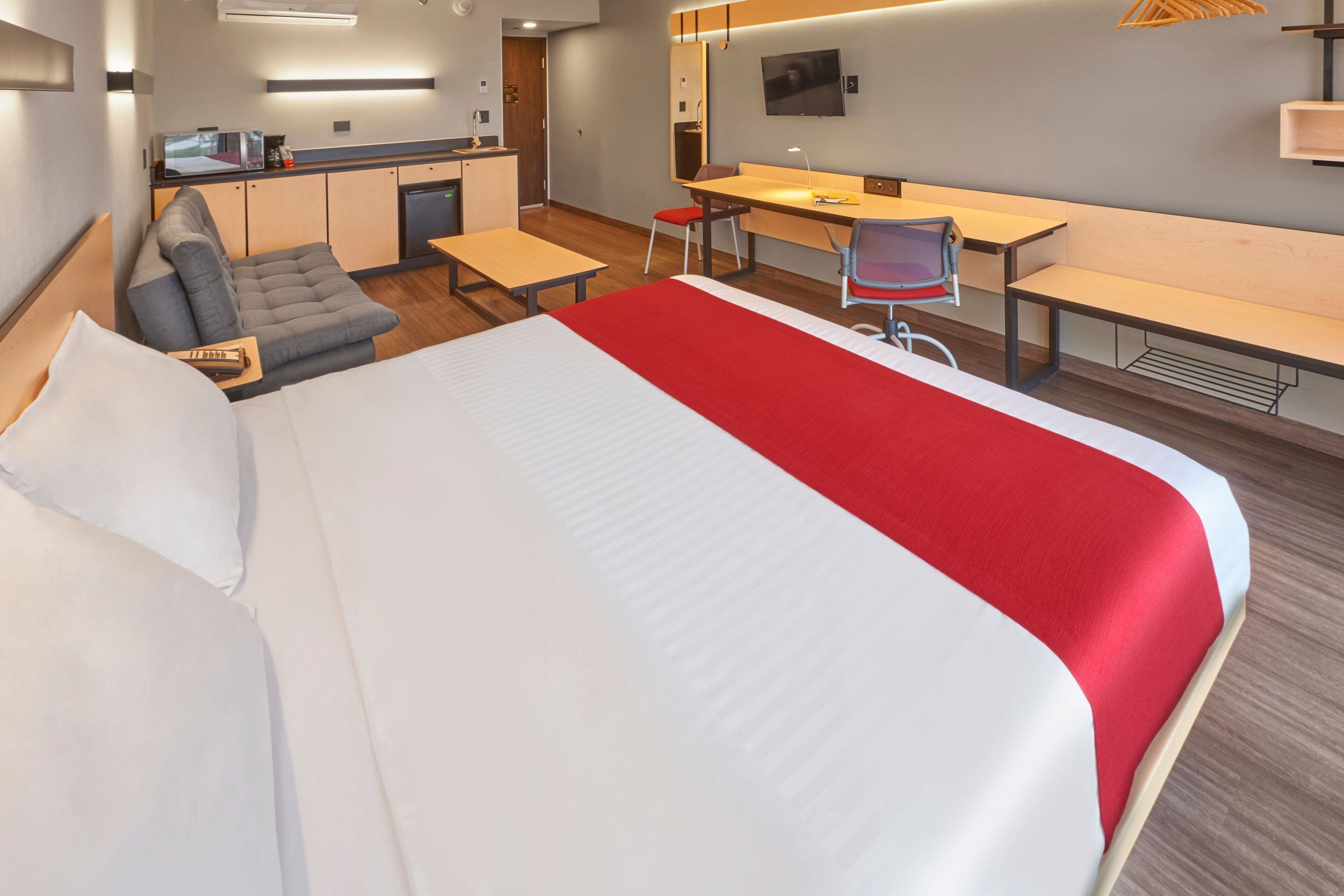 A modern hotel room with a large bed, a desk, a chair, a sofa, and a TV.