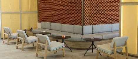 A modern lounge area with a curved seating arrangement, wooden chairs, and small round tables.