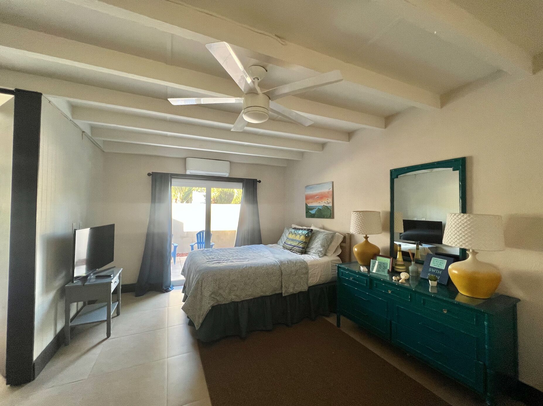 A bedroom with a bed, a TV, a desk, a dresser, and a ceiling fan.