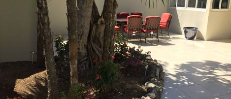 Eine Terrassenfläche mit Tisch und Stühlen, umgeben von einem Garten mit Palmen und blühenden Pflanzen.
