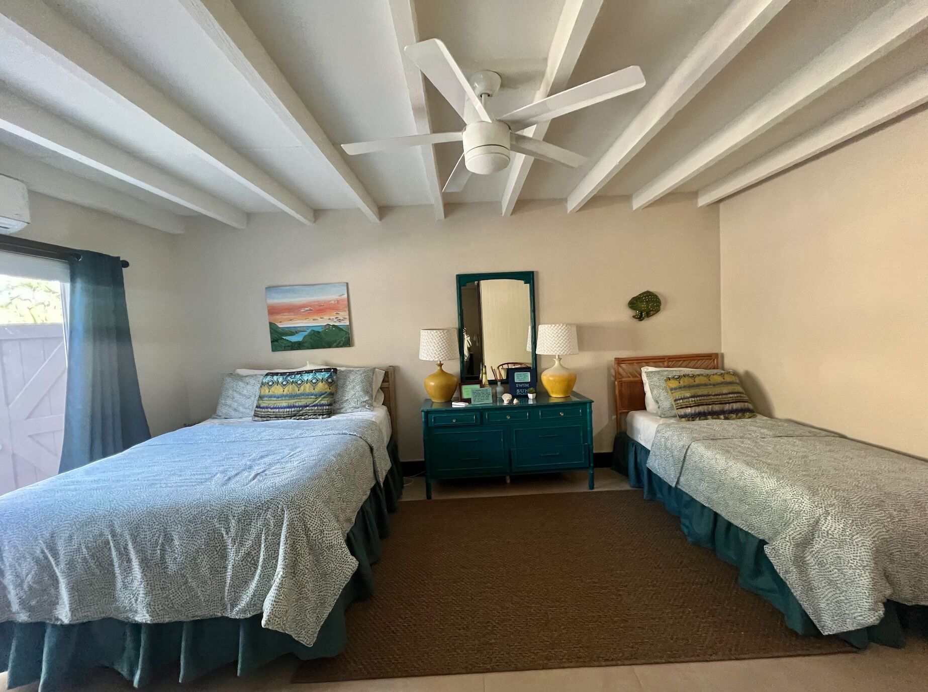 Une chambre avec deux lits, un ventilateur de plafond, une commode, un miroir et un tableau au mur.