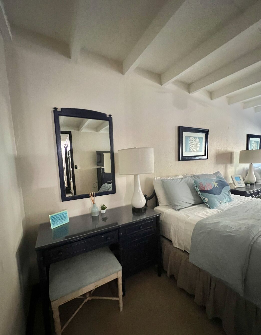 Een hotelkamer met een bed, nachtkastjes, een bureau, een stoel, een spiegel en lijstwerken aan de muur.