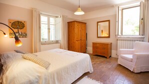 Un dormitorio con cama, armario de madera, cómoda, silla, espejo y ventana.