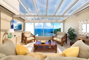 Una habitación soleada con un amplio ventanal con vistas al océano, amoblada con un sofá, dos sillones y una mesa de centro.
