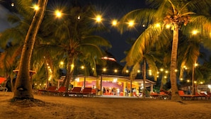 A beachside restaurant with outdoor seating, palm trees, and string lights. - POCO POCO Villa - Caribbean Golf, Diving & Beach Holiday Home (Blue Bay Golf & Beach Resort, Willemstad, Curacao)