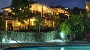 A two-story building with a pool, surrounded by lush greenery and palm trees. - POCO POCO Villa - Caribbean Golf, Diving & Beach Holiday Home (Blue Bay Golf & Beach Resort, Willemstad, Curacao)