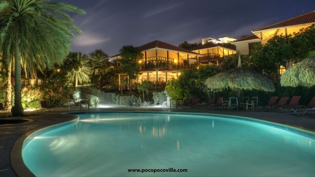 A nighttime view of a resort with a swimming pool, palm trees, and a building with a balcony overlooking the pool. - POCO POCO Villa - Caribbean Golf, Diving & Beach Holiday Home (Blue Bay Golf & Beach Resort, Willemstad, Curacao)