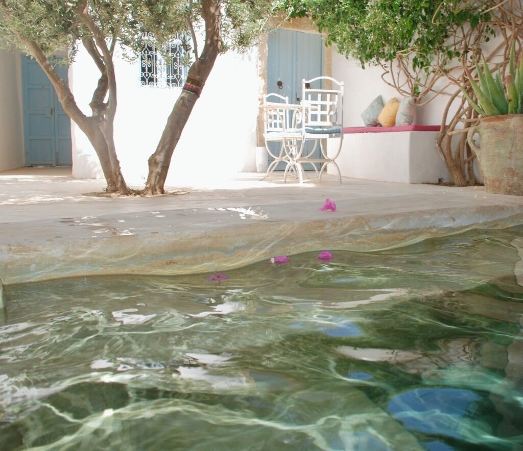 A clear pool with a white metal table and chairs, surrounded by trees and a potted plant.