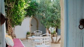 An outdoor seating area with a white metal table and chairs, a pink cushioned bench, and potted plants.