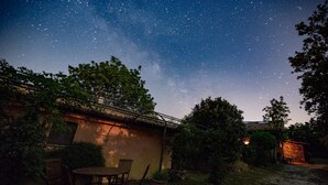 Un patio con una mesa y sillas, un edificio con tejado de baldosas y un cielo nocturno estrellado.