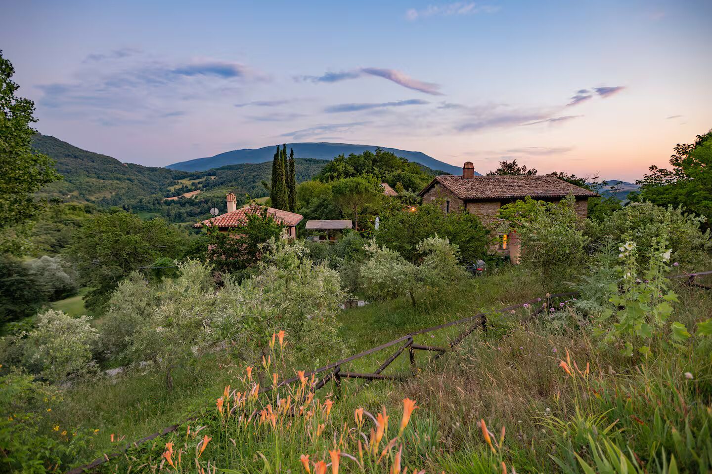 A rural landscape with traditional stone houses, lush greenery, and distant hills.
