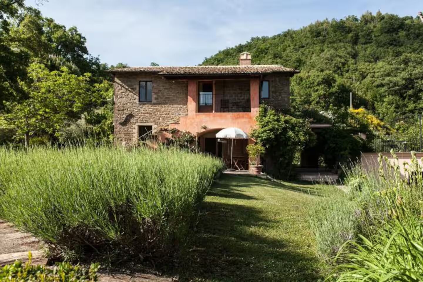 A stone house with a tiled roof, surrounded by lush greenery and a well-maintained lawn.