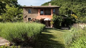 Una casa de piedra con techo de tejas, rodeada de exuberante follaje y un césped bien cuidado.