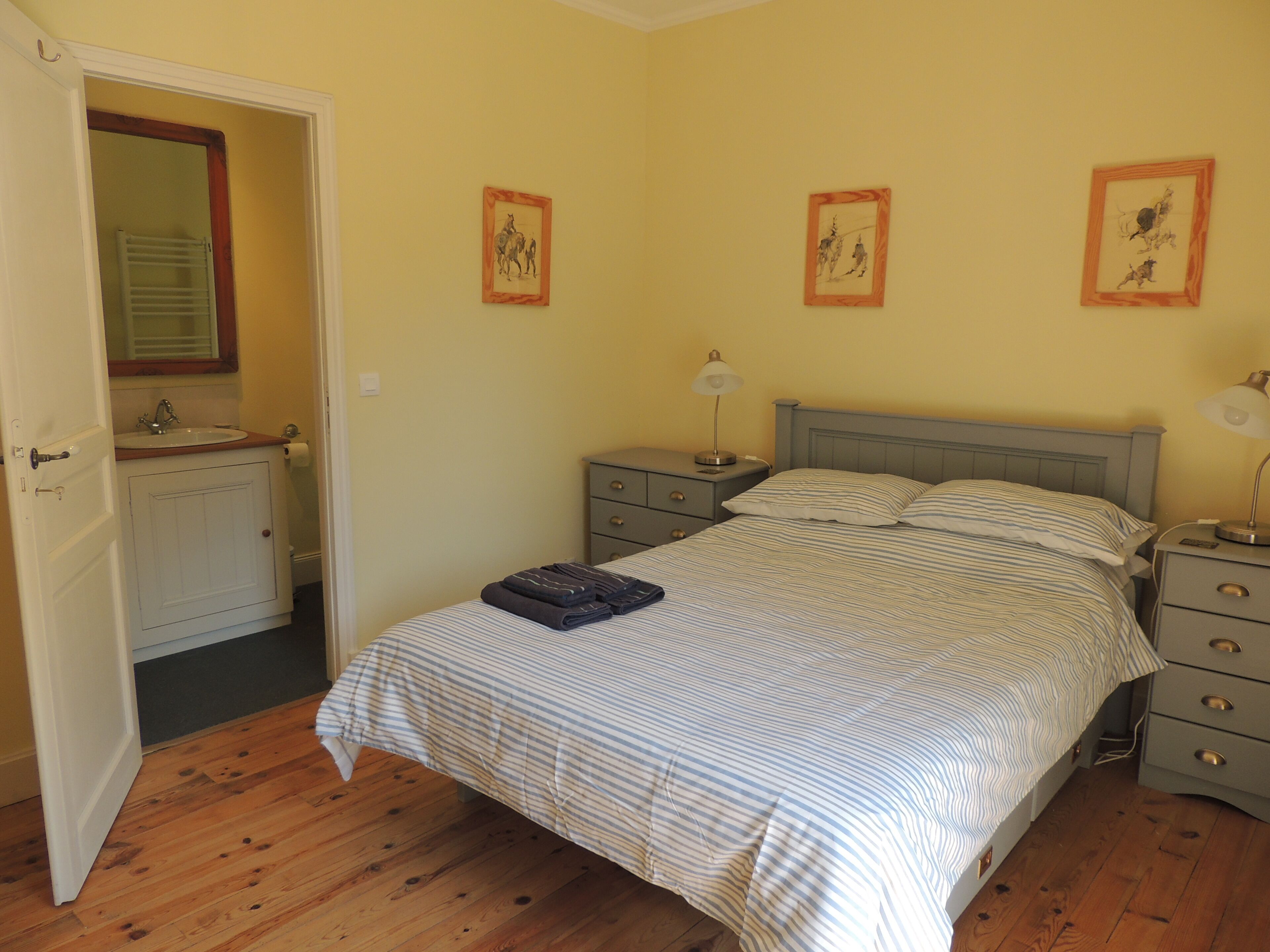 A bedroom with a bed, two bedside tables, a nightstand, a dresser, a mirror, and a door leading to a bathroom.