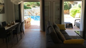 Un soggiorno con divano, tavolo da pranzo e sedie. Vista su una zona esterna con piscina e vegetazione.