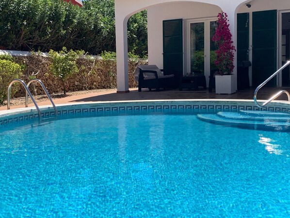 Una piscina cristallina con gradini che vi conducono all'interno, circondata da un portico coperto con mobili da esterno.