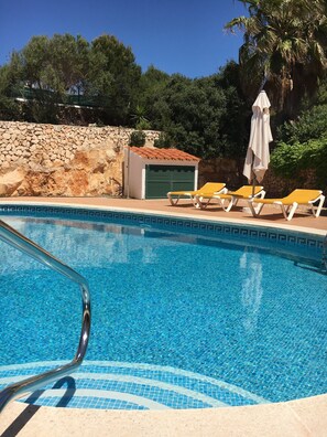 Una piscina cristallina dai piastrelle azzurre, circondata da lettini e un muro in pietra.