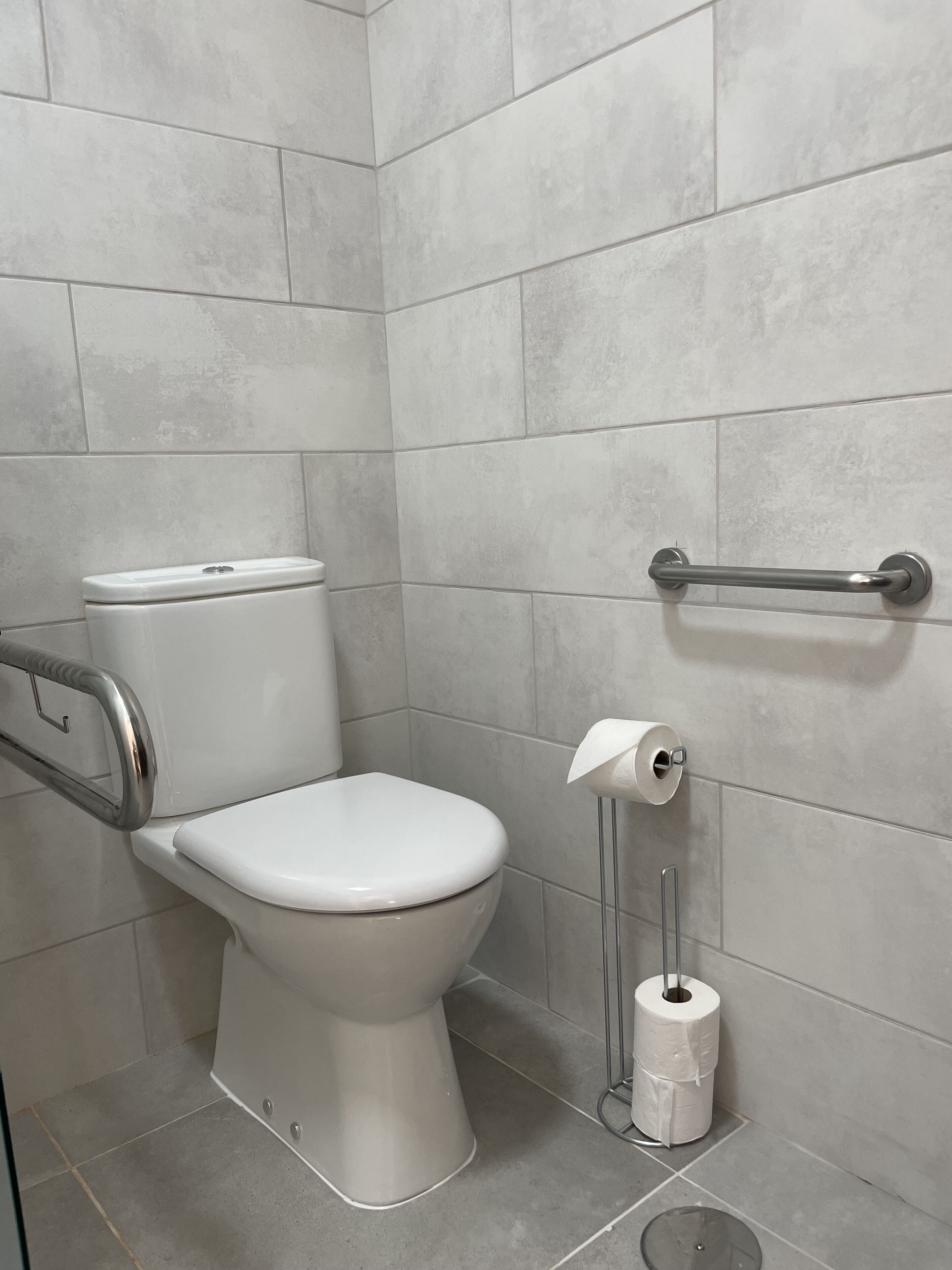 Casa de banho moderna com sanita branca, barra de apoio e porta-papel higiénico.