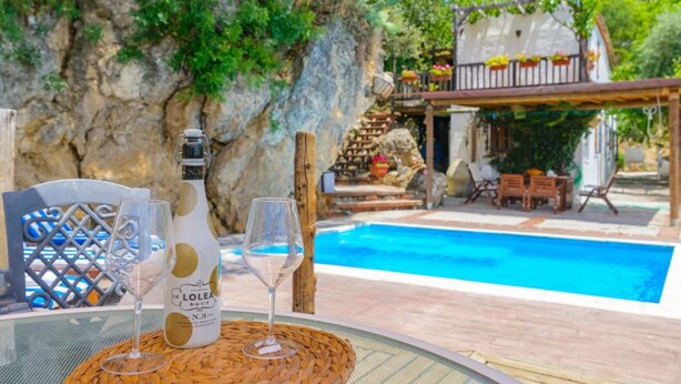 Une scène de bord de piscine avec une bouteille de vin Lolea Brut, deux verres et une table en osier.