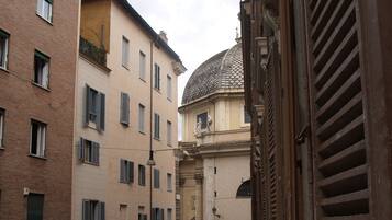 A narrow street with buildings on either side, a row of parked scooters, and a small balcony with a stone balustrade.