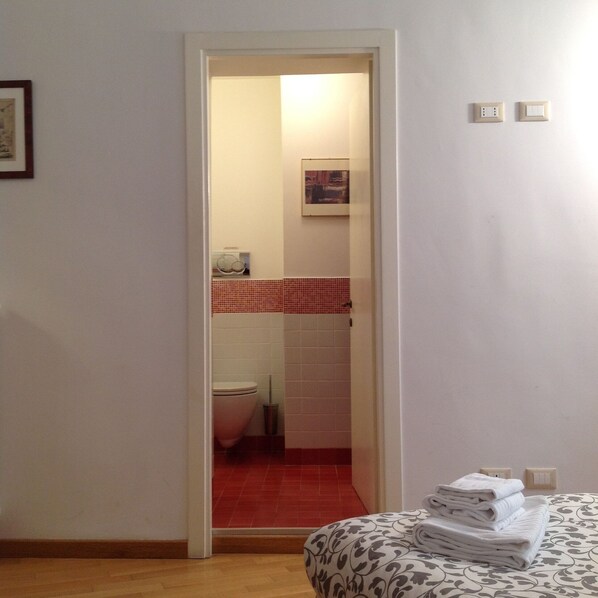A hotel room with a wooden floor, a bed with a patterned bedspread, a small bedside table, and a wall-mounted light switch. - terrace viadelloca35 (Roma)