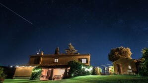 Ein Haus mit geneigtem Dach, einer kleinen Veranda und einem gut beleuchteten Garten bei Nacht.