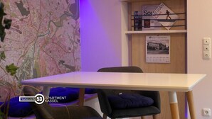 Una habitación con un mapa en la pared, una mesa, sillas y estanterías con libros y un póster.