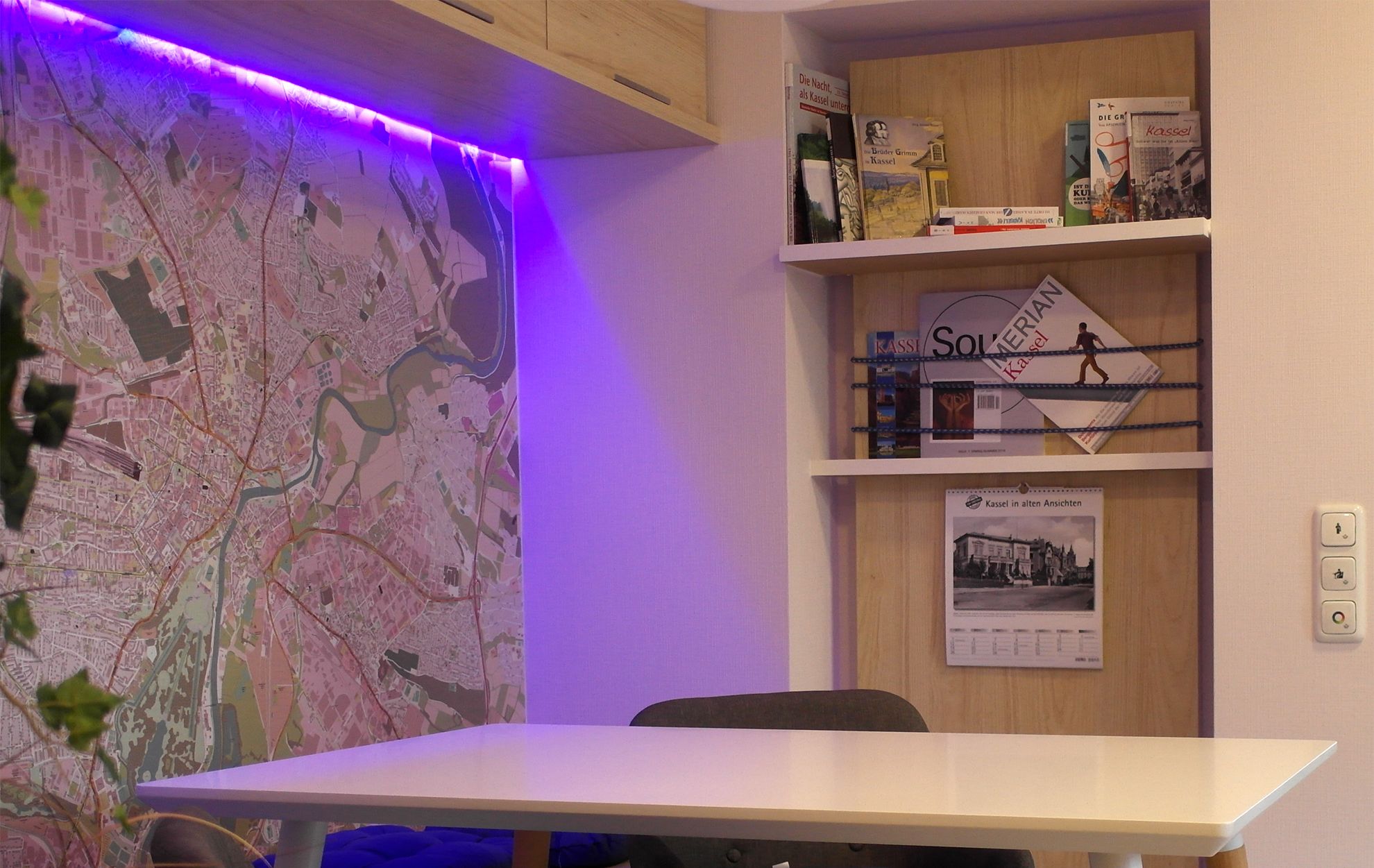 Une pièce avec une carte accrochée au mur, une table, des chaises et des étagères remplies de livres et une affiche.