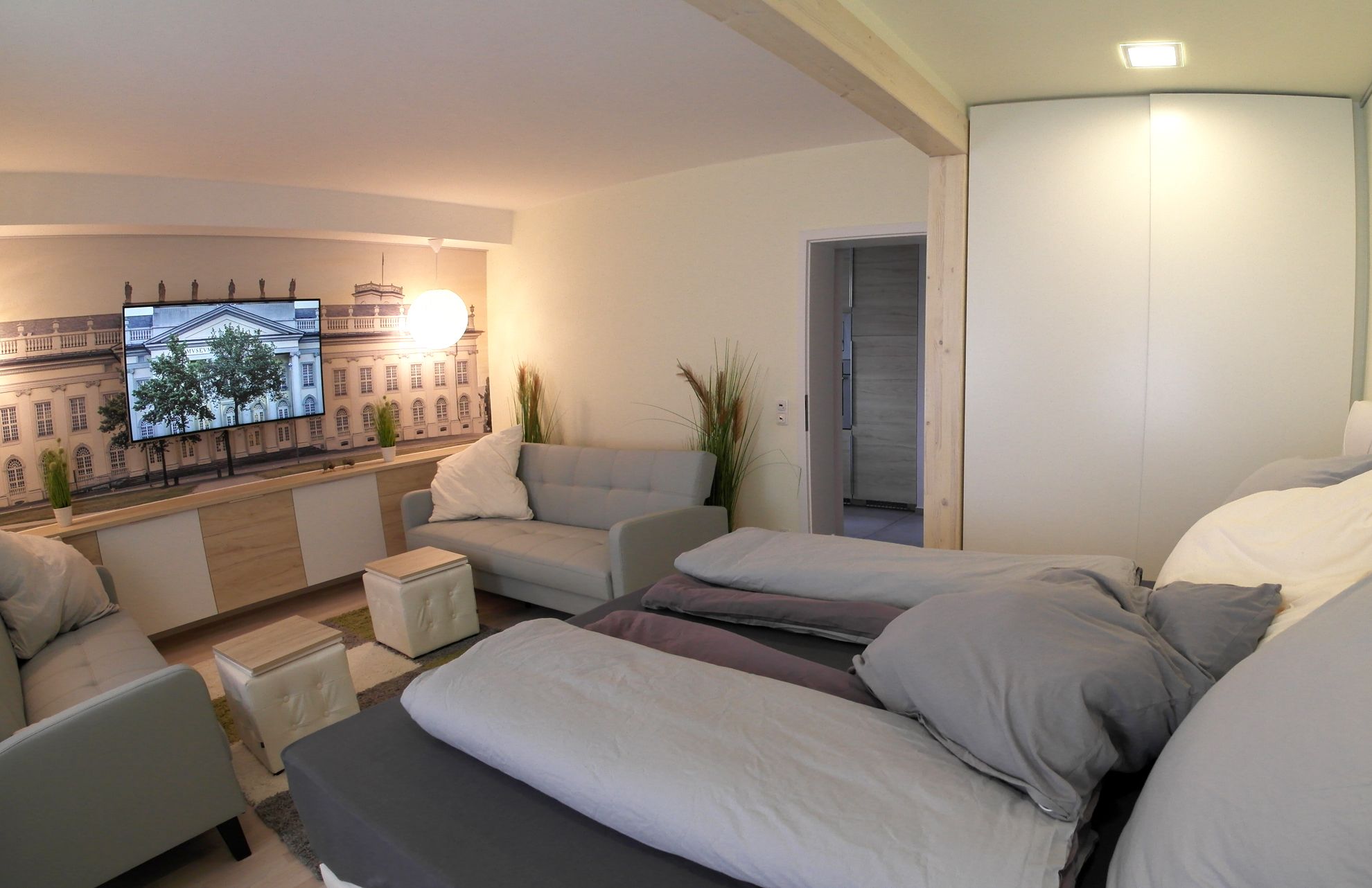 Un appartement moderne comprenant un canapé, deux lits, une télévision et donnant sur un immeuble.