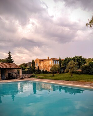 A stone villa with a swimming pool, surrounded by lush greenery and a cloudy sky. - GITE A CLANSAYES in Drôme Provençale, in the farmhouse "La bergerie des sources".  (Clansayes)