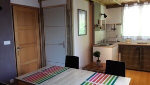 A compact kitchen with a wooden table, chairs, and a small dining area. - Gite au figuier - studio Duplex 2/4 people (Arbois)