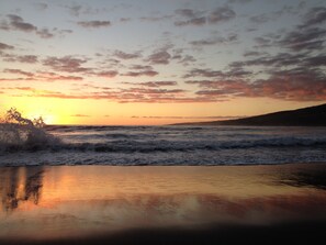 A beach at sunset with waves crashing onto the shore and a clear sky.
