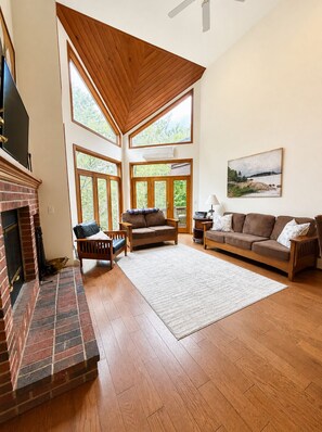 A spacious living room with a fireplace, wooden flooring, and large windows allowing natural light. - C7 Beautifully appointed slopesideCrawford Ridge end unit townhome with fireplaces, yard (Bretton Woods)