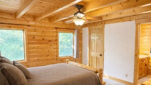 A wooden cabin bedroom with a bed, two windows, a door, and a ceiling fan.
