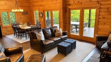 A log cabin interior with a leather sofa, ottomans, dining table, chairs, and large windows.