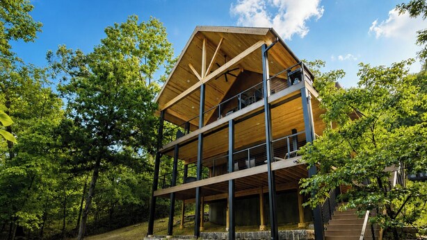 A multi-level wooden cabin with a stone staircase, outdoor seating, and a fire pit.