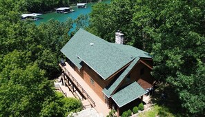 A cabin with a green roof, surrounded by dense trees, and a dock extending into a lake.