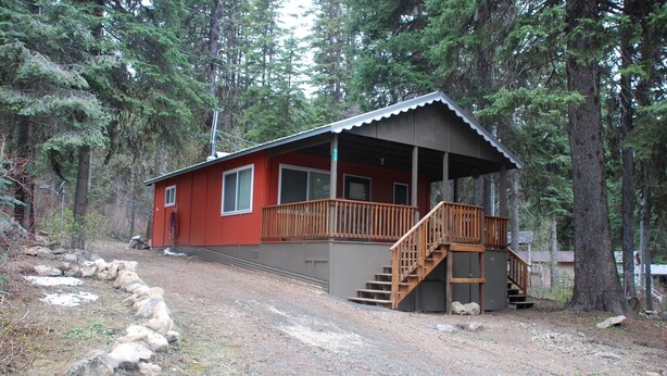 A cabin with a wooden deck and a staircase leading to a porch.