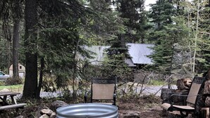 A rustic outdoor seating area with a metal fire pit surrounded by rocks, a wooden bench, and a chair.