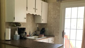 A kitchen with white cabinets, a granite countertop, a coffee maker, and a window with a view.